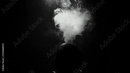 the silhouette of a man on a dark background exhales clouds of smoke