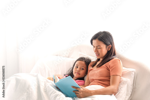 Mother reading the book with daughter at home during virus quarantine. Family reading a book together on free time.