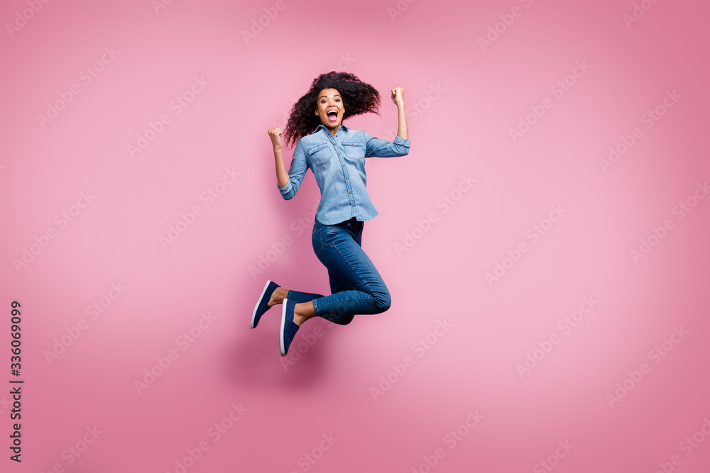 Full body photo of delighted afro american girl hear lottery win news impressed scream yeah jump raise fists feel euphoria emotions wear casual style outfit isolated pink color background