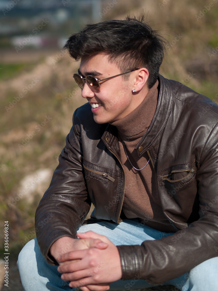 junger Mann in Lederjacke und Sonnenbrille sitzt draußen junger Mann in Lederjacke und Sonnenbrille sitzt draußen