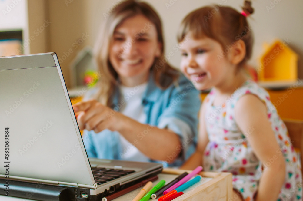 Smiling mother and toddler daughter looking at the notebook indoor Smiling mother and toddler daughter looking at the notebook indoor