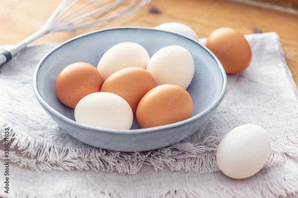Close up of six white and brown eggs in a light blue bown placed on a dish-cloth with a metal mixer in the background Close up of six white and brown eggs in a light blue bown placed on a dish-cloth with a metal mixer in the background