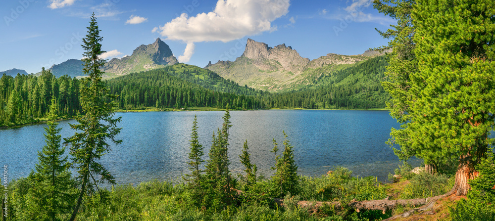 Panoramic view of a picturesque mountain lake. Sayan Mountains, Ergaki, travels in Russia. Summer greens and rocky peaks. Siberian nature.