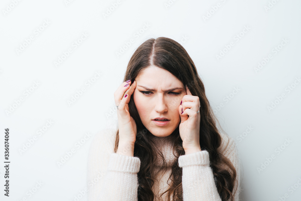 Young woman holding her head in pain suffering from a headache on a white background Young woman holding her head in pain suffering from a headache on a white background