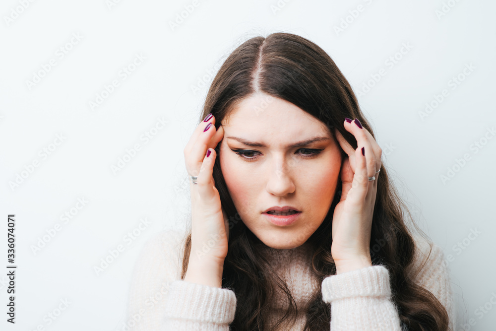 Young woman holding her head in pain suffering from a headache on a white background Young woman holding her head in pain suffering from a headache on a white background