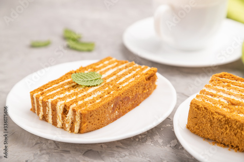 Homemade honey cake with milk cream and mint with cup of coffee on a gray concrete background. Side view, selective focus.