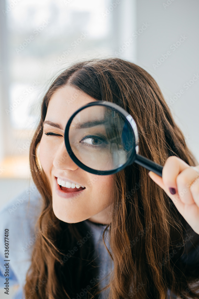 Young beautiful woman with magnifying glass near the window. Young beautiful woman with magnifying glass near the window.