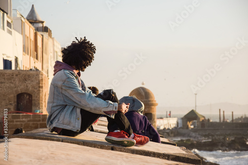 Joven con pelo estilo afro sentado junto al mar contemplando el atardecer en Essaouira
