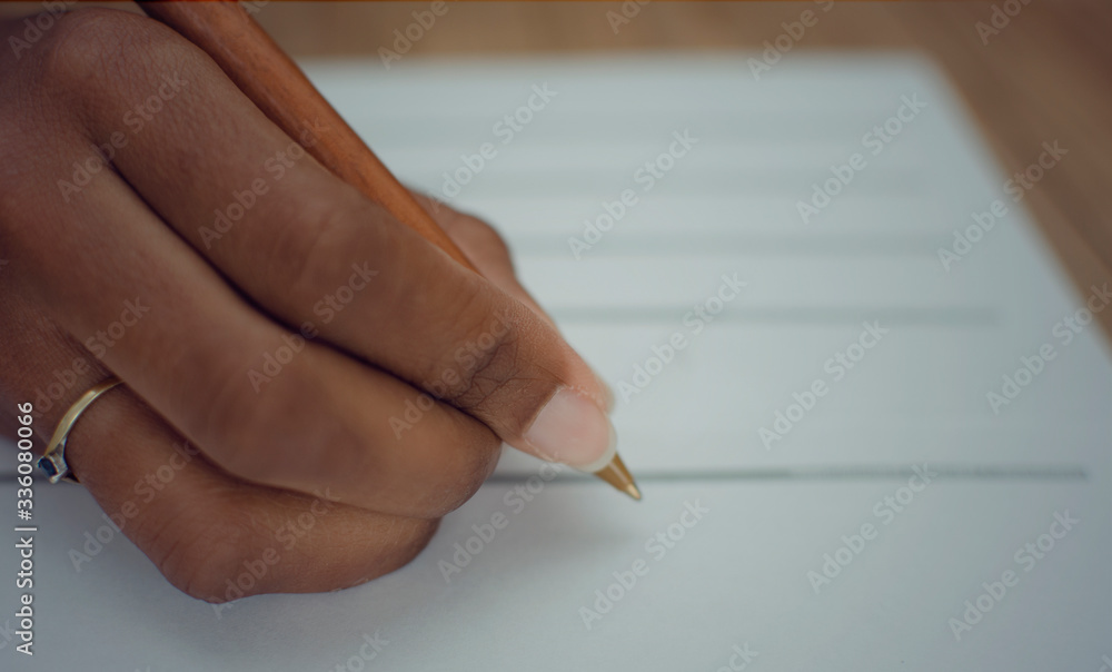 Closeup of the right hand of a black woman filling a paper document. Selective focus on her index finger. Closeup of the right hand of a black woman filling a paper document. Selective focus on her index finger.