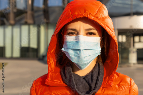 A woman wears a protective mask against allergies, viruses, air pollution. Climate change concept. Portrait of a young woman in a medical mask from a coronavirus in a red jacket on the street.