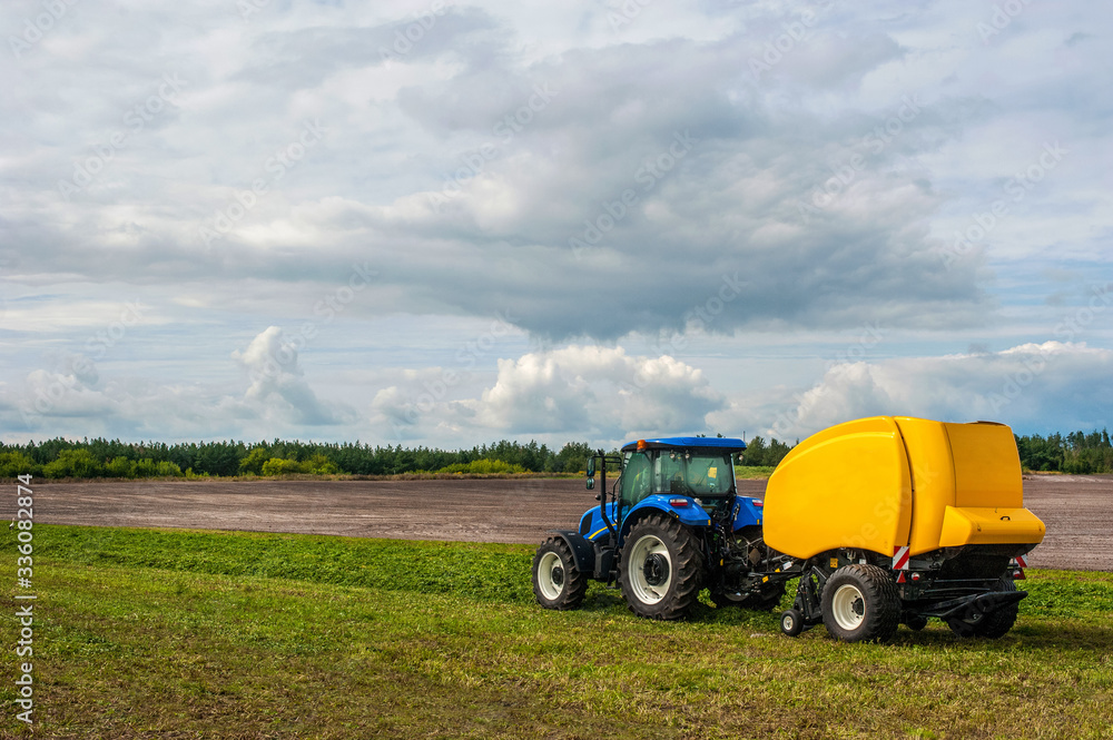 Fototapeta premium new blue tractor with baler in motion at field at agro work