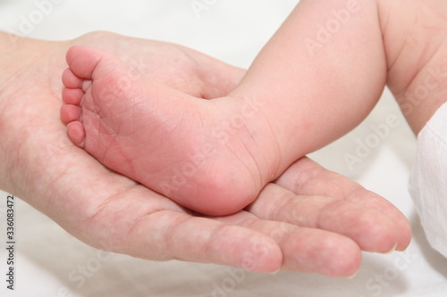 a small newborn baby in the arms of its mother, the mother holds the newborn's legs in her hands © MaxМ
