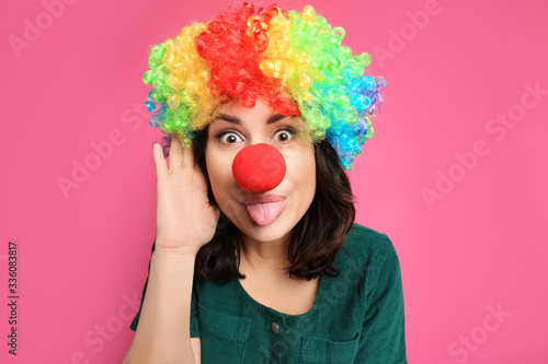 Funny woman with rainbow wig and clown nose on pink background. April fool's day