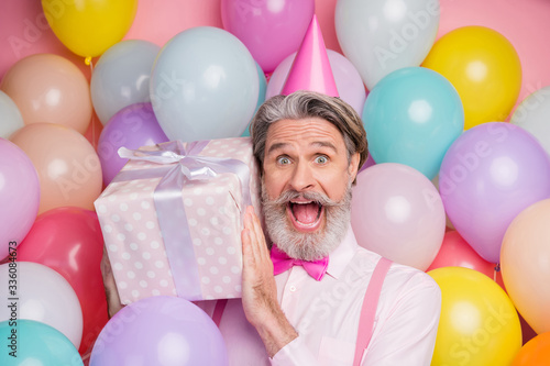 Close-up portrait of his he nice attractive cheerful cheery funky grey-haired mature man having fun holding in hands giftbox isolated over pink pastel color background © deagreez