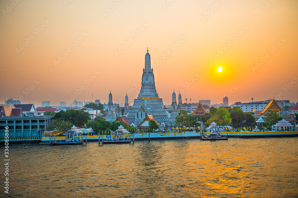 Beautiful Temple of Dawn or Wat Arun and Thonburi west bank of Chao Phraya River at sunset with shining sun. Bangkok, Thailand