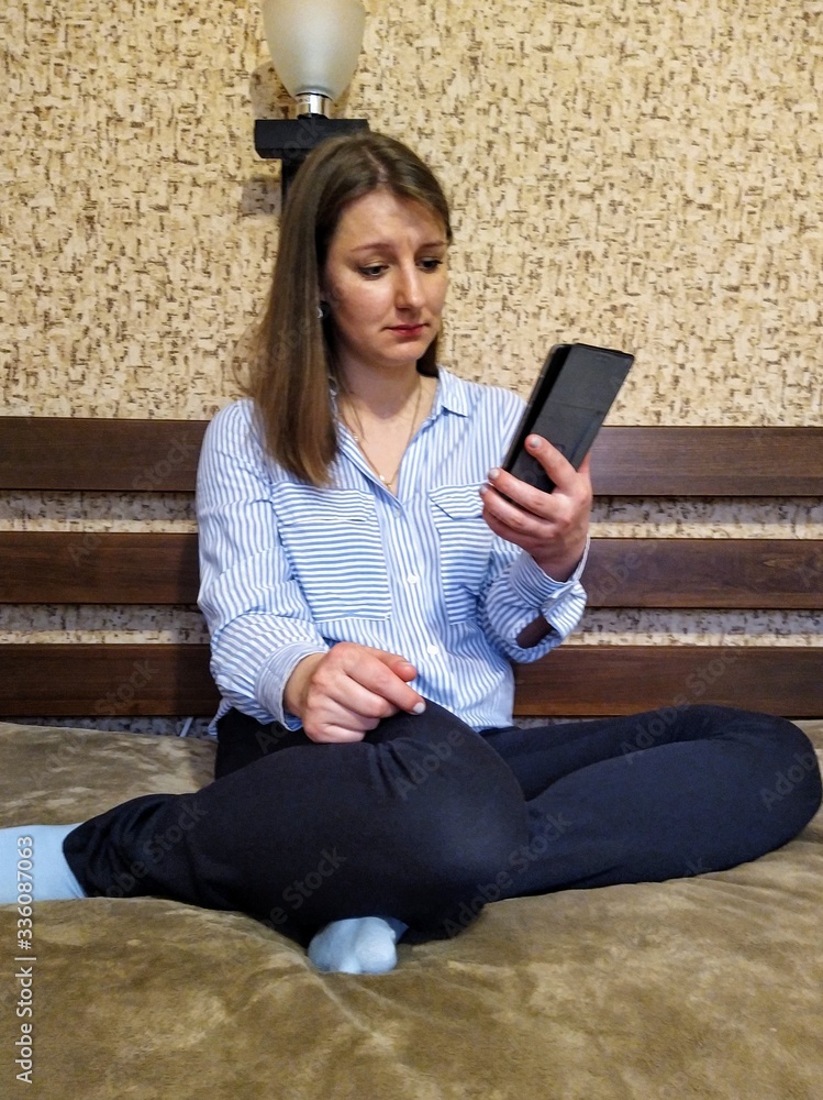 Obraz premium Upset european woman sit on bed and use smartphone