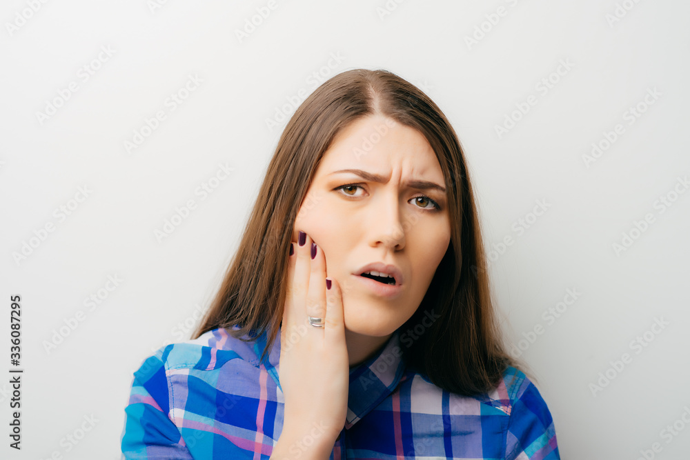 Teen woman pressing her bruised cheek with a painful expression as if she's having a terrible tooth ache. Teen woman pressing her bruised cheek with a painful expression as if she's having a terrible tooth ache.