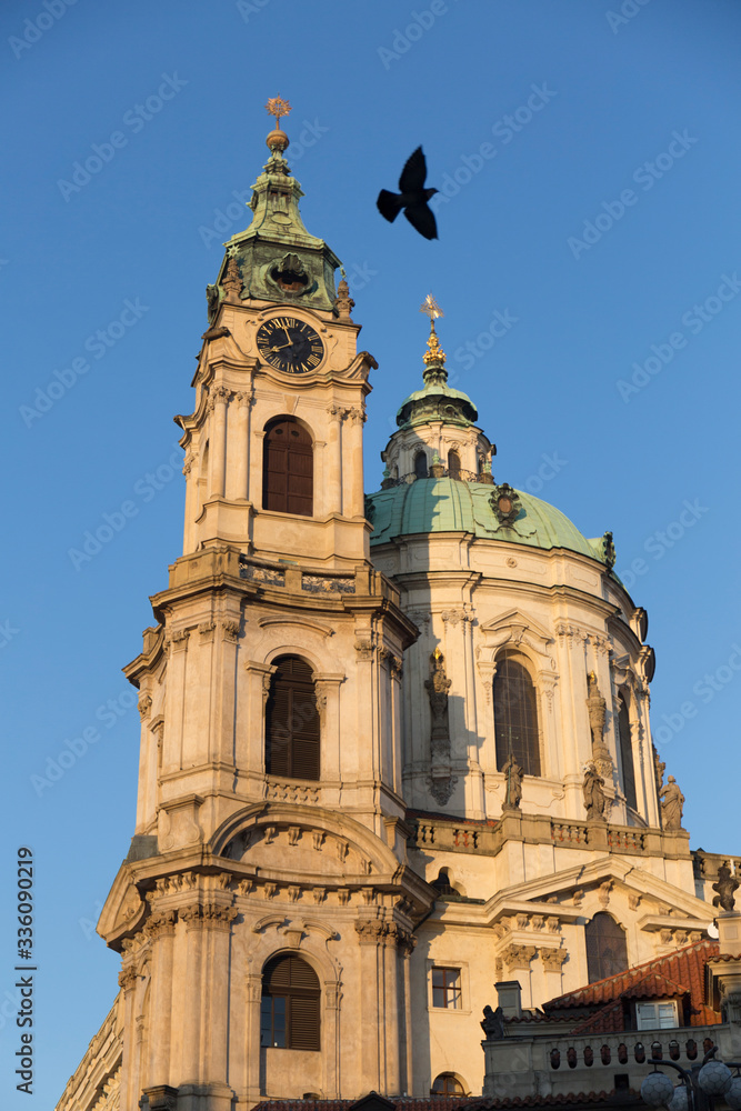 facade of a historic building in the city of Prague, cream-colored facade, with green domes, a bird flies over the building