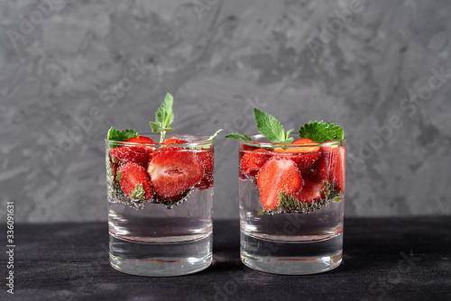 Infused water with strawberry and mint in sparkling glasses on wood black table background, copy space. Cold summer drink. Mineral water photo