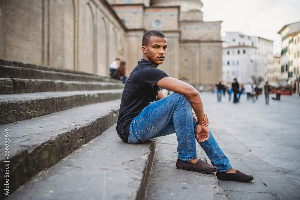 Portrait of young man in Florence, Italy - Millennial taking a break sitting on the stairs of a square with the church Portrait of young man in Florence, Italy - Millennial taking a break sitting on the stairs of a square with the church