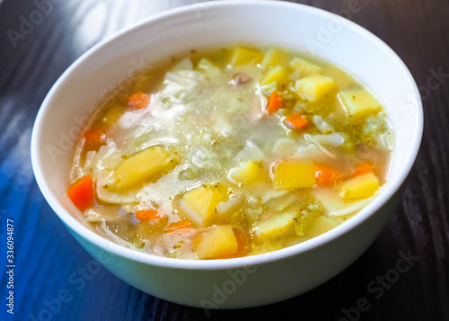 Soup in a white plate of broccoli, carrots, potatoes and square gluten-free pasta . Entree
