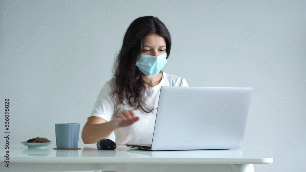 The girl works from home during quarantine. Corona virus pandemic. A girl in a surgical mask works on a laptop and drinks coffee. Distant work The girl works from home during quarantine. Corona virus pandemic. A girl in a surgical mask works on a laptop and drinks coffee. Distant work