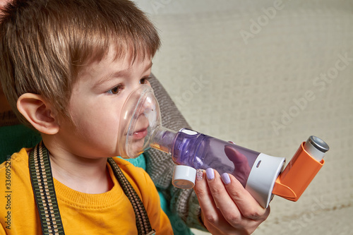 Fényképezés A small boy who suffering from illness bronchial asthma getting breathing treatment from mother with aerosol inhaler