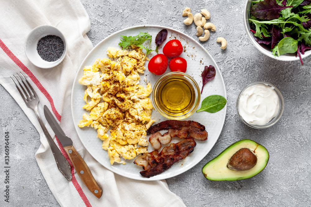 Keto breakfast with scramble eggs, avocado, tomatoes, cream and bacon