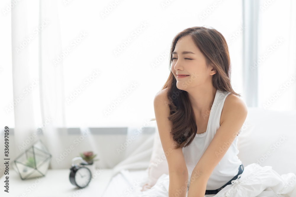 Beautiful Asian Smiling woman with eyes closed relaxing in bed at home. Portrait of Happy Charming Shy girl in white pajamas with long hair wake up and breathing air on morning. Carefree Beautiful Asian Smiling woman with eyes closed relaxing in bed at home. Portrait of Happy Charming Shy girl in white pajamas with long hair wake up and breathing air on morning. Carefree
