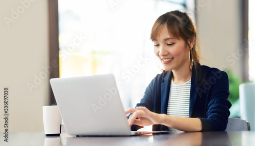 Happy young businesswoman using laptop computer doing online shopping at cafe. Smiling beautiful Asian woman sitting and working at her workplace. Lifestyle, Technology, Internet © eggeeggjiew