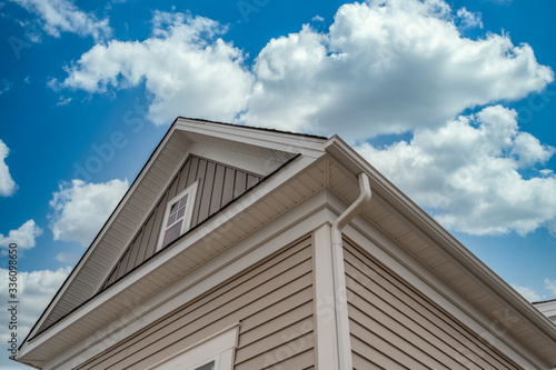 Gable with horizontal vinyl siding, white frame gutter guard system, fascia, drip edge, soffit, on a pitched roof attic at a luxury American single family home neighborhood USA with cloudy blue sky
