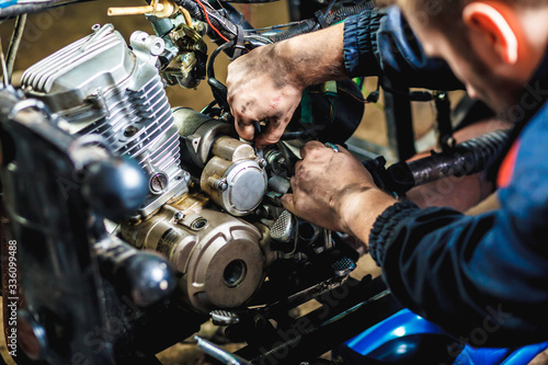 Specialist in coveralls working with motorized bicycles at repair garage. Motorcycle repair