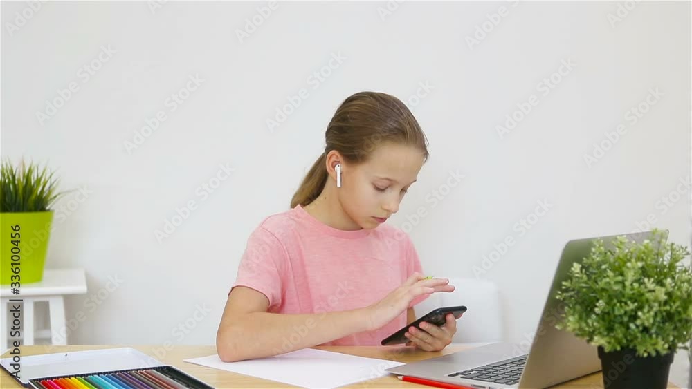 Serious schoolgirl sitting at table with laptop and textbook and doing homework. Study from home Serious schoolgirl sitting at table with laptop and textbook and doing homework. Study from home