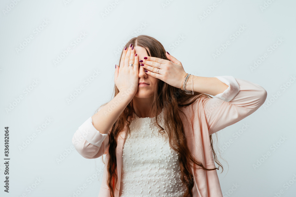 on a gray background young girl closes eyes with her hands on a gray background young girl closes eyes with her hands