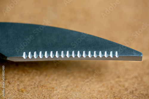 One blade with notches from scissors for cutting fish and meat on the wooden background close up photo