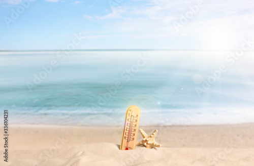 Thermometer, sea star and sandy beach on sunny day