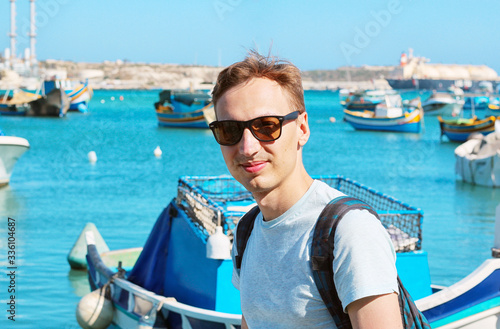 Marsaxlokk harbor fishing boats colourful Malta, Young man sitting at water front. Banner for a tourist company.  © frecca