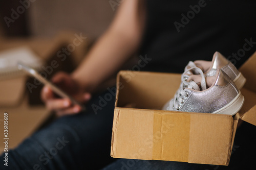 Young woman open new parcel with clothes. Woman hepl to sell secound hand goods photo