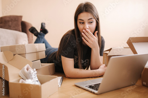 Young woman doing online shopping at home. Female lying on the wooden floor with different parcel. Woman using laptop and credit card