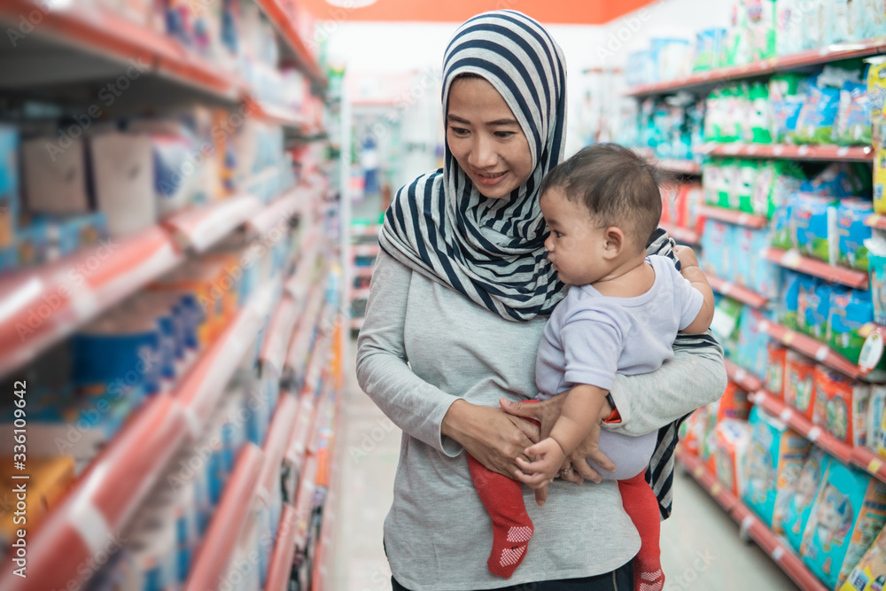 muslim asian mother buying baby product while carrying her daughter muslim asian mother buying baby product while carrying her daughter