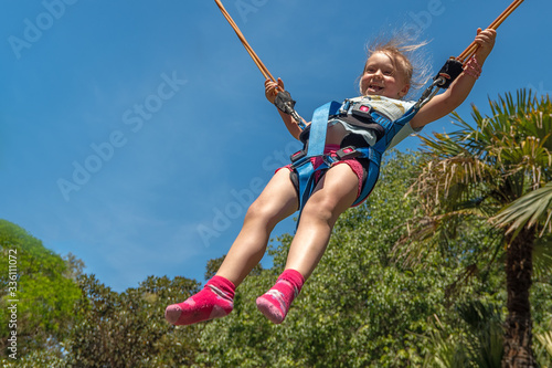 Happy girl jumping on a bungee trampoline in the park. Background of palm trees and blue sky.