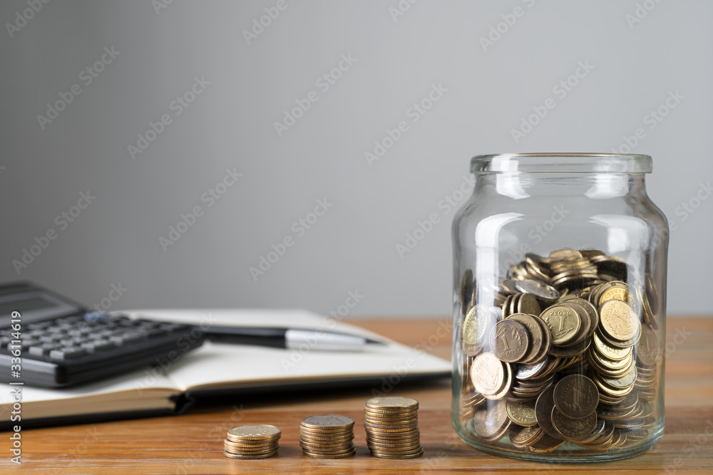 Coins in a jar and stacks of change with savings notepad and calculator in a background. Money collecting or accounting abstract concept. Copy space.