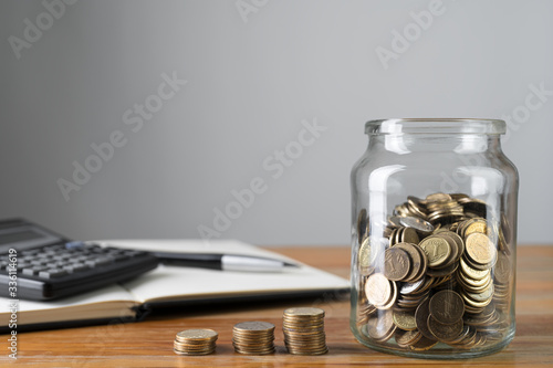 Obraz na płótnie Coins in a jar and stacks of change with savings notepad and calculator in a background. Money collecting or accounting abstract concept. Copy space. w salonie