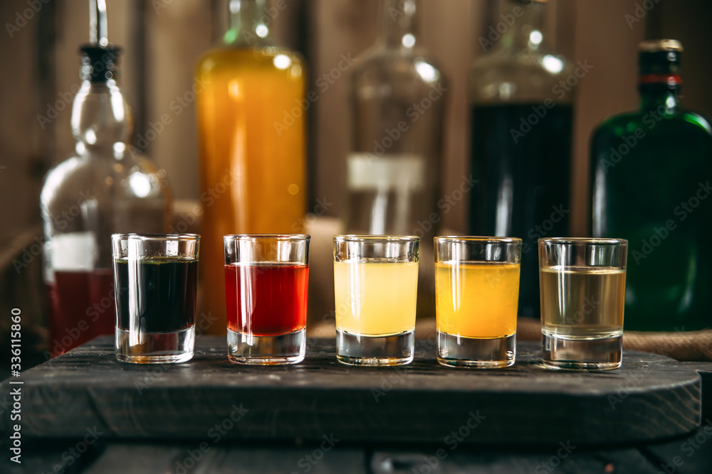 Variety of alcohol bevegares in shots and bottles behind on the black wooden board, side view, horizontal Variety of alcohol bevegares in shots and bottles behind on the black wooden board, side view, horizontal