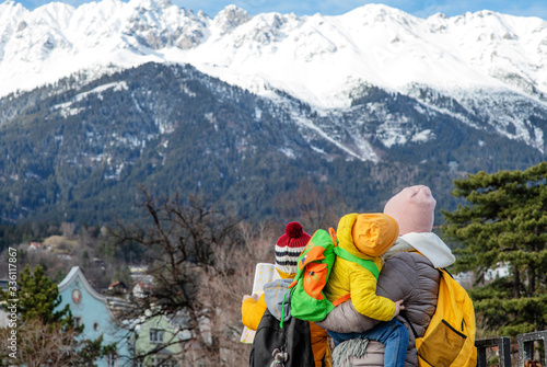 The family looks at the mountains. Mom holds the baby in her arms and looks at the card that her child holds. Alps in Austria stand in the background. Family vacation concept