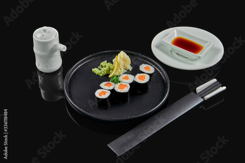 Traditional maki sushi rolls with salmon on a black plate in composition with soy sauce and chopsticks on a black background. Japanese food. Photo for the menu