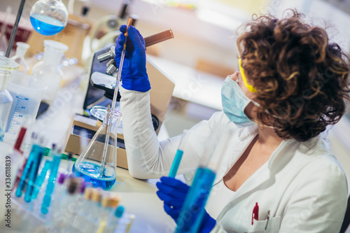 Young attractive female scientist in protective eyeglasses and gloves using test tube with blue liquid sample substance probe in the scientific chemical research laboratory