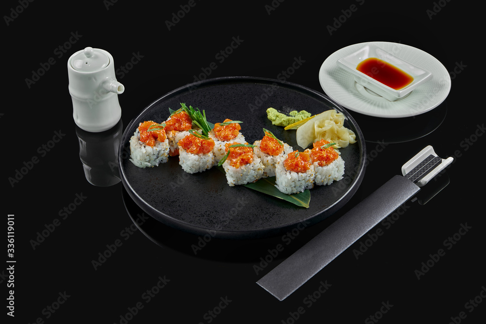 Spicy sushi rolls with rice, norms, mayonnaise, tobiko caviar and salmon on a black ceramic plate on a black background. Japanese traditional food. Spicy sushi rolls with rice, norms, mayonnaise, tobiko caviar and salmon on a black ceramic plate on a black background. Japanese traditional food.