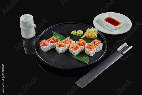 Spicy sushi rolls with rice, norms, mayonnaise, tobiko caviar and tuna on a black ceramic plate on a black background. Japanese traditional food.
