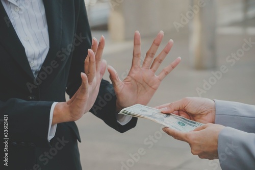 Businessman or businesswoman holding stack of money in hand offering bribe, hand gesture rejecting the proposal.
